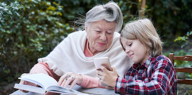 Фотография семьи: бабушка и внучка изучают своё генеалогическое древо на мобильном устройстве